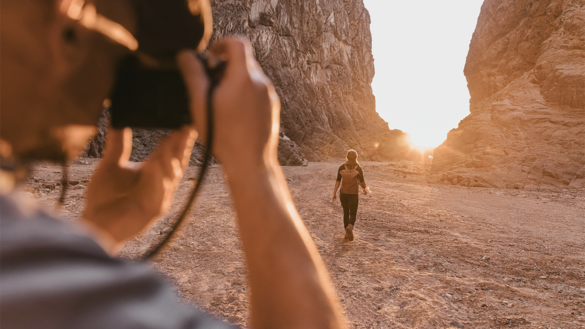 A person being photographed walking between two large rock fronts