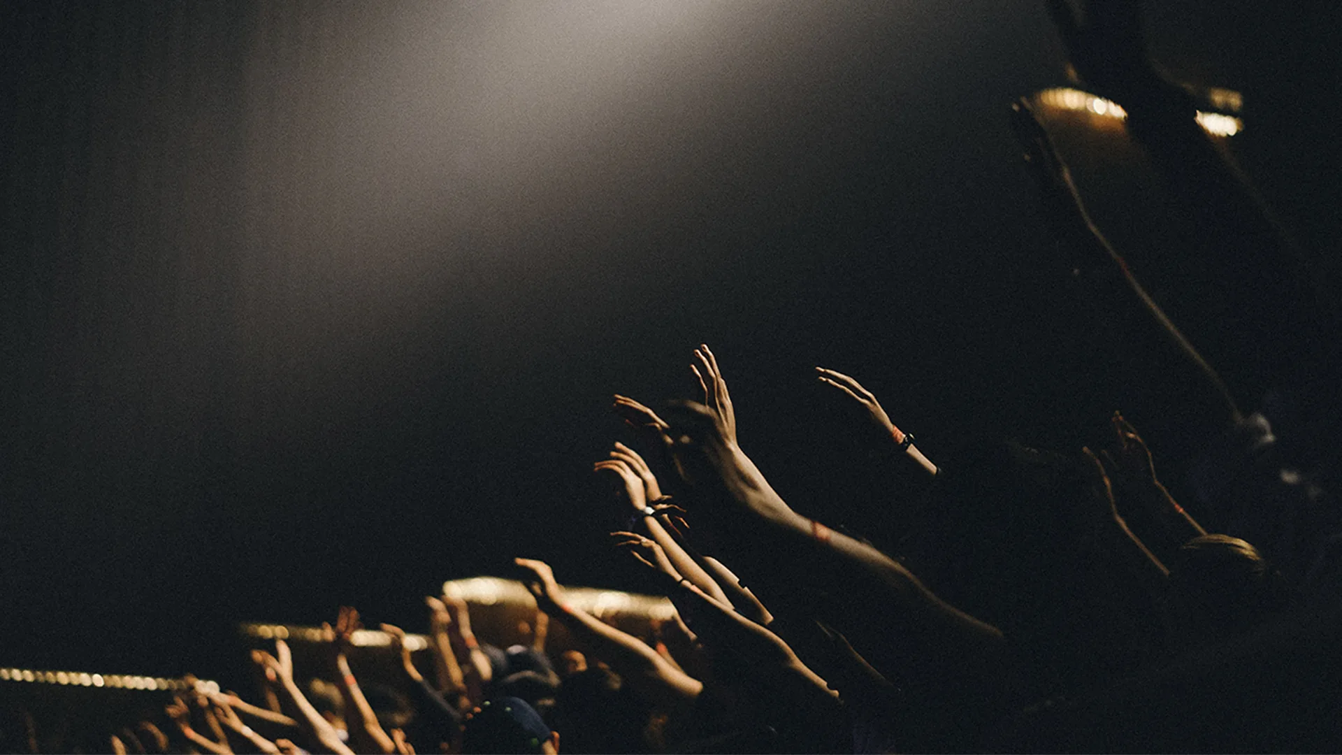 Fans at the front of a concert with their hands up in the air at night