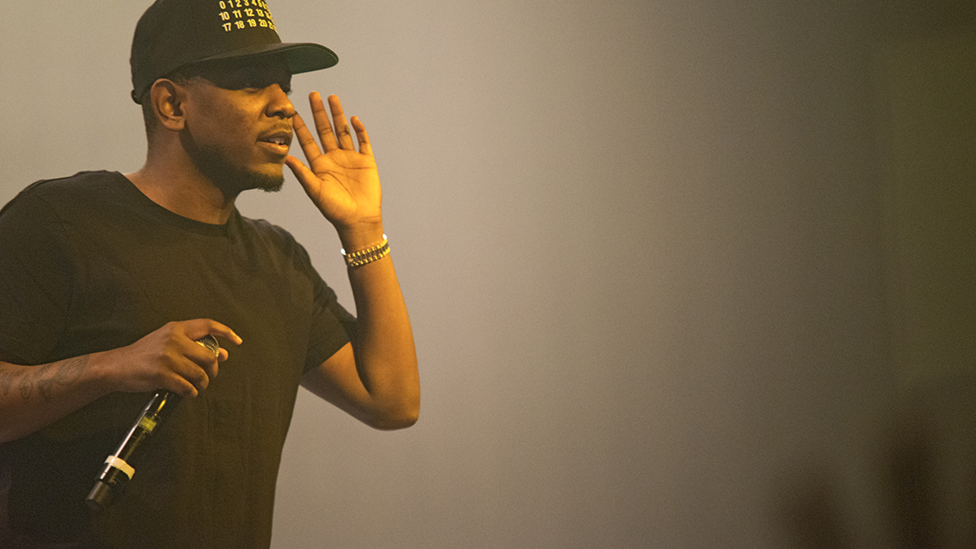 Kendrick Lamar on stage with his hand by his face in a call and response motion, he is lit with yellow lights