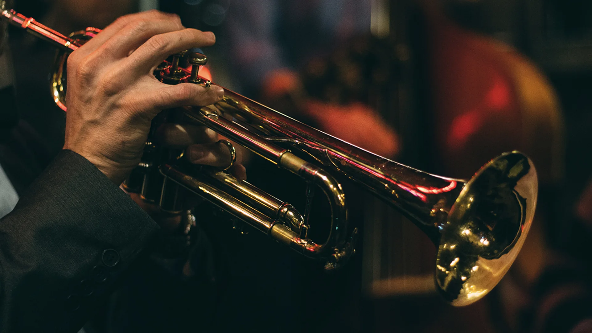 Close up of musician's hands playing trumpet on black background.