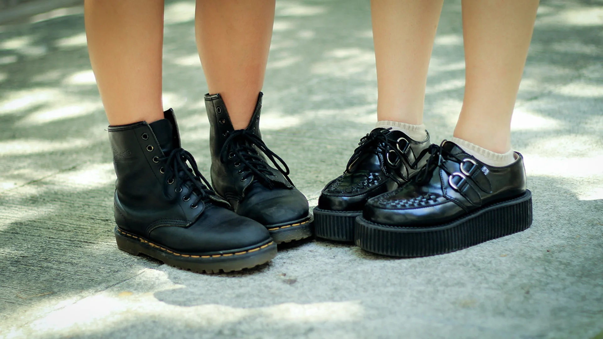 Two people standing next to each other. The person on the left is wearing Doctor Martens and the person on the right is wearing Creepers