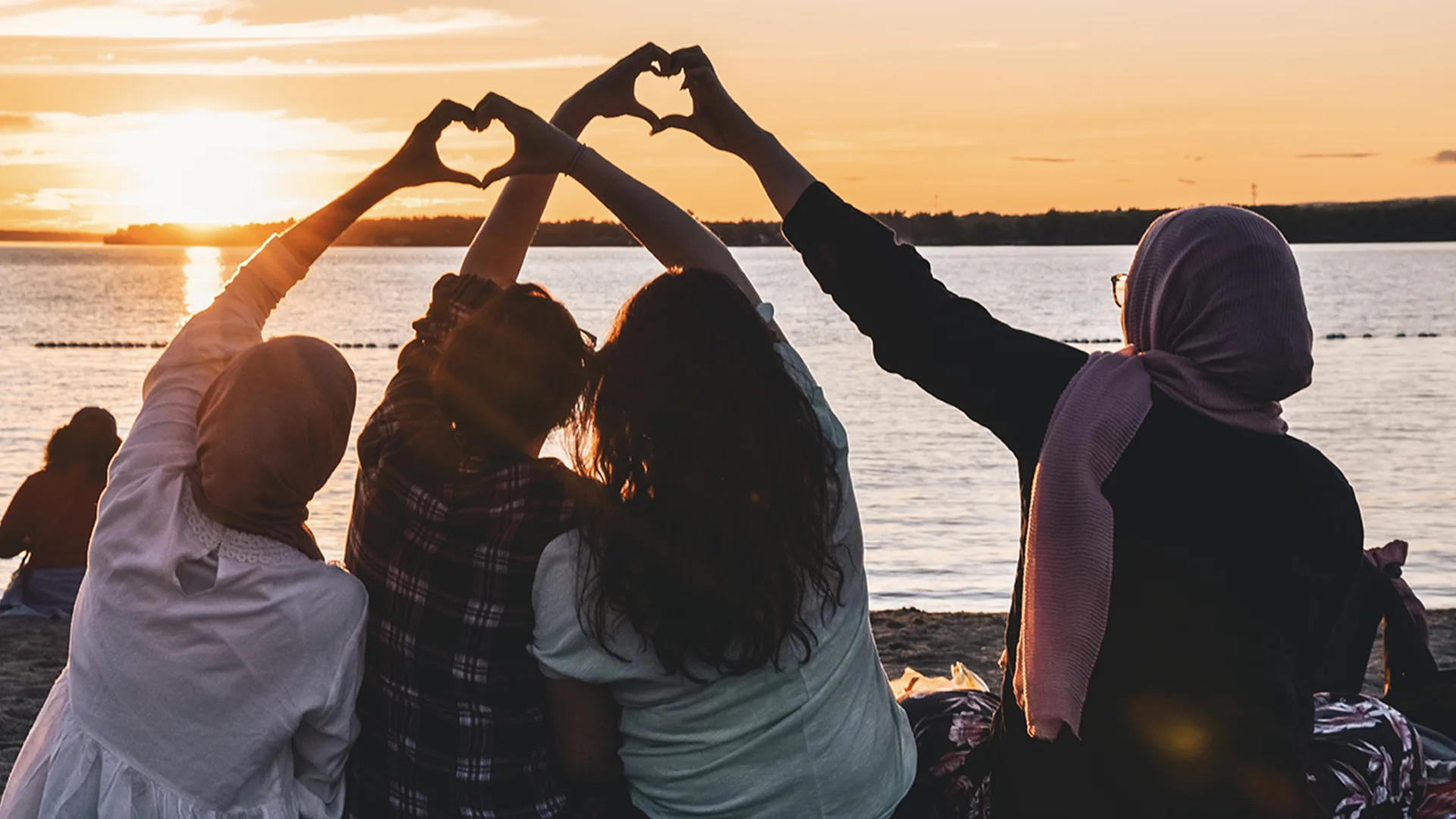 Four people on a beach forming hearts with their hands