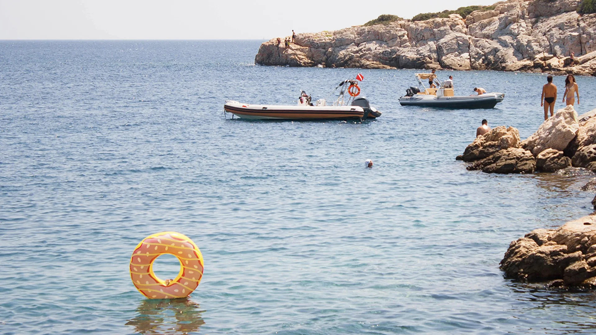 A sea with two boats and people standing on the rocks