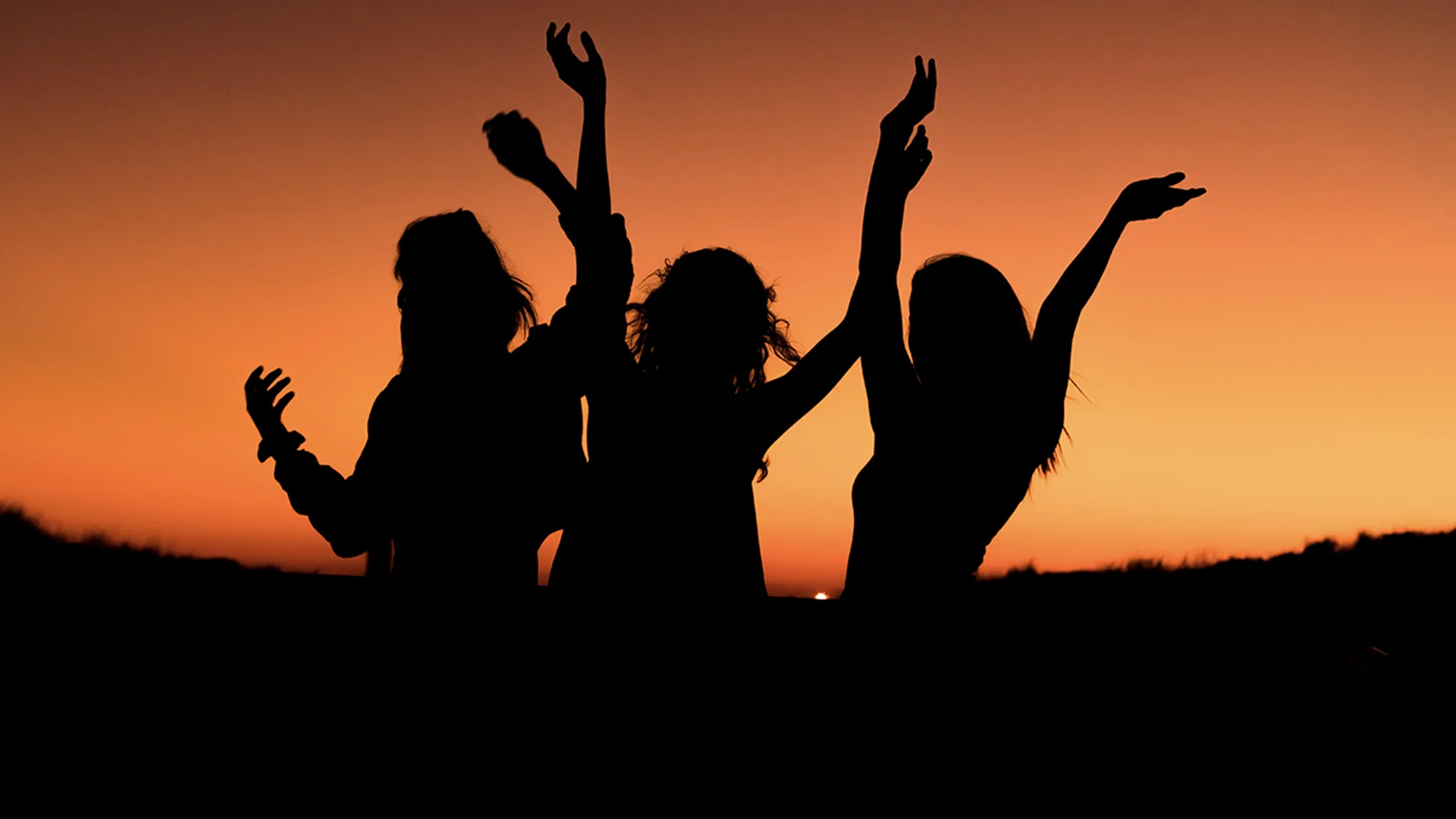 A group of friends with their arms raised in a sunset