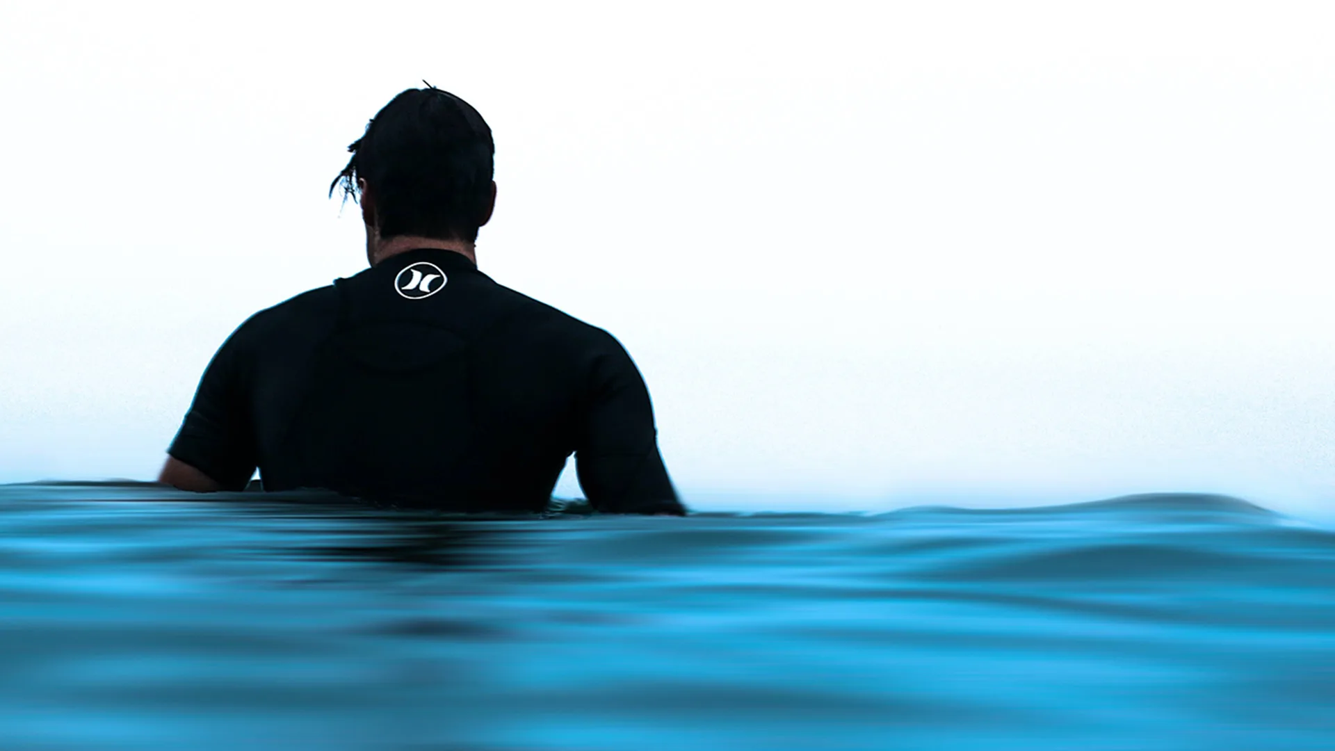 Back of a man in sea wearing a wetsuit