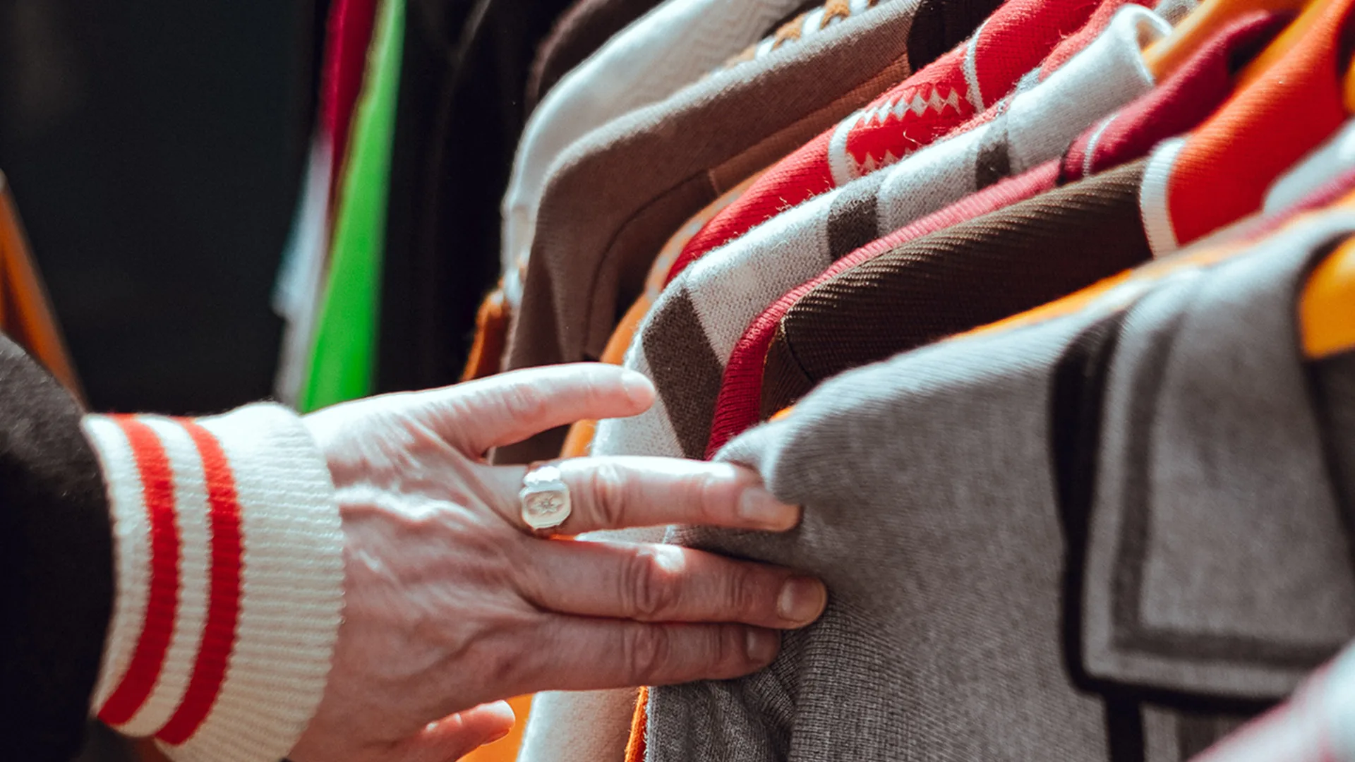 Man's hand selecting bright coloured tops on a rail