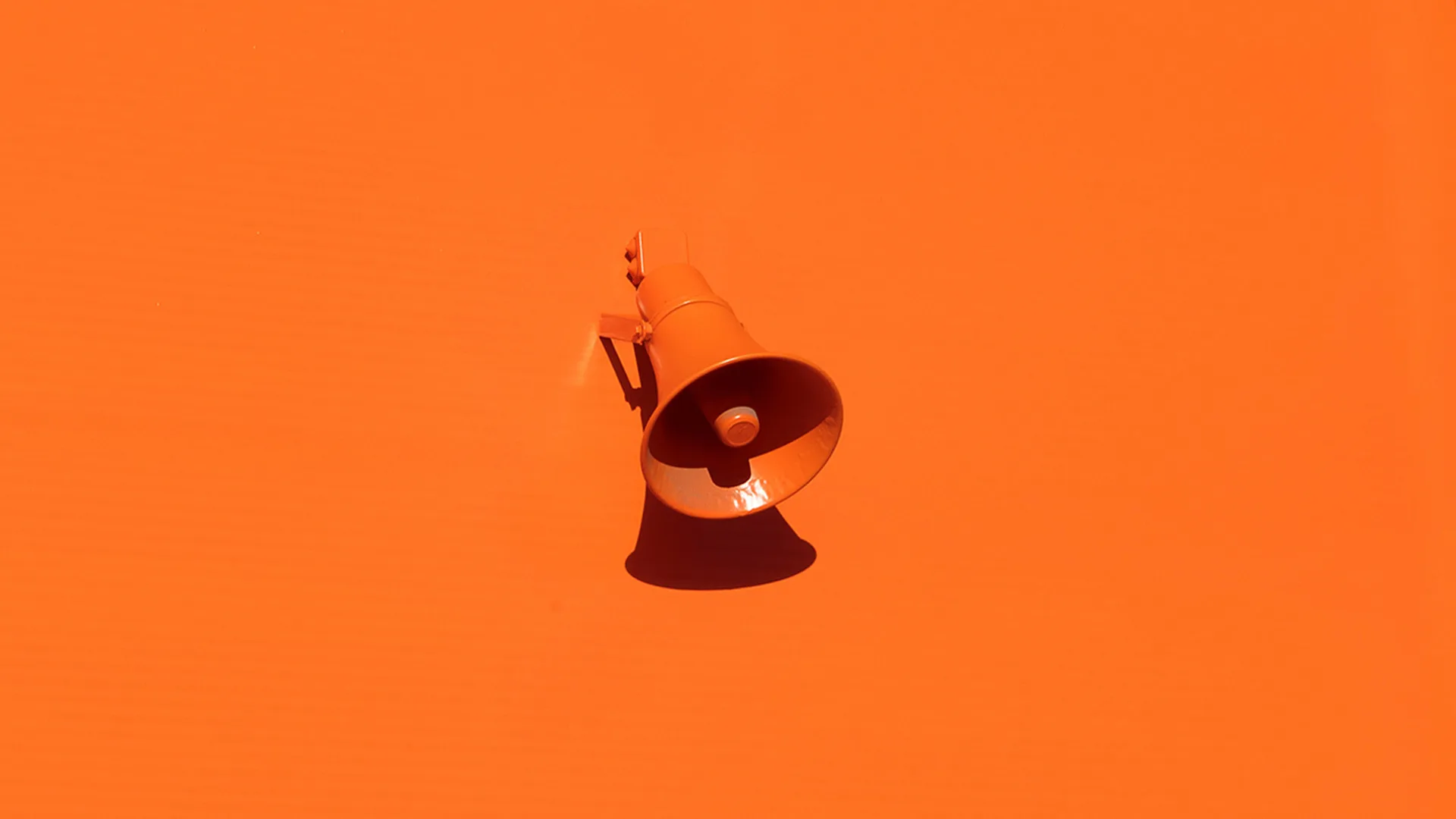 Orange loudspeaker hanging on orange wall.