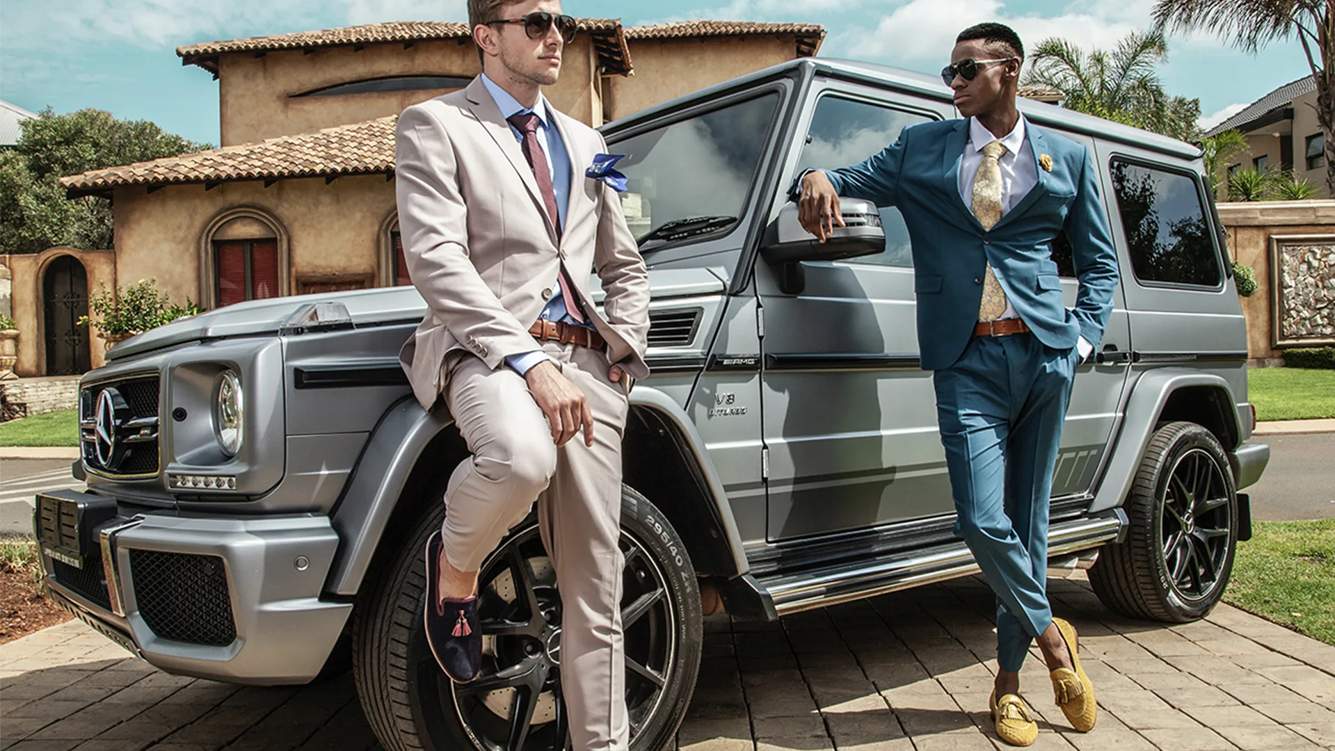 Two men in suits in front of an expensive car