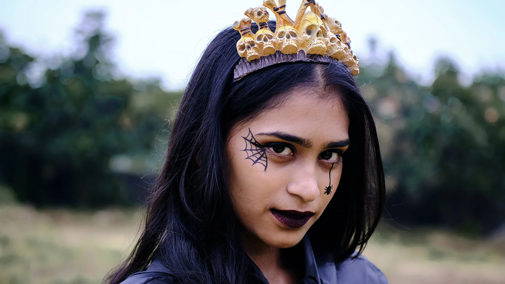 Girl dressed up with crown, cape and spiderweb painted on her cheek