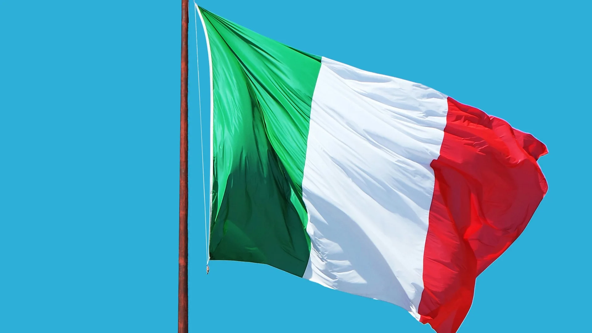 Photograph of the Italian flag blowing in the wind against a blue sky