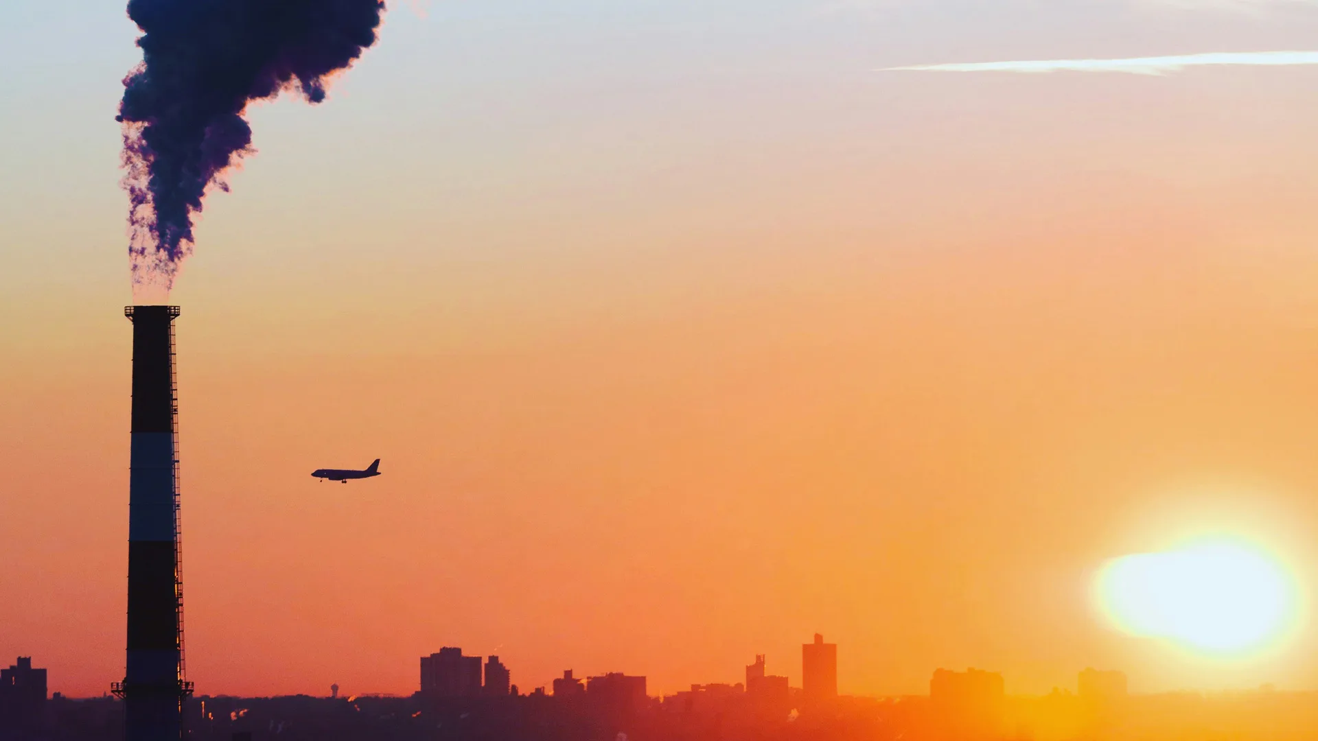 Photograph of a factory pipe billowing smoke against a sunset