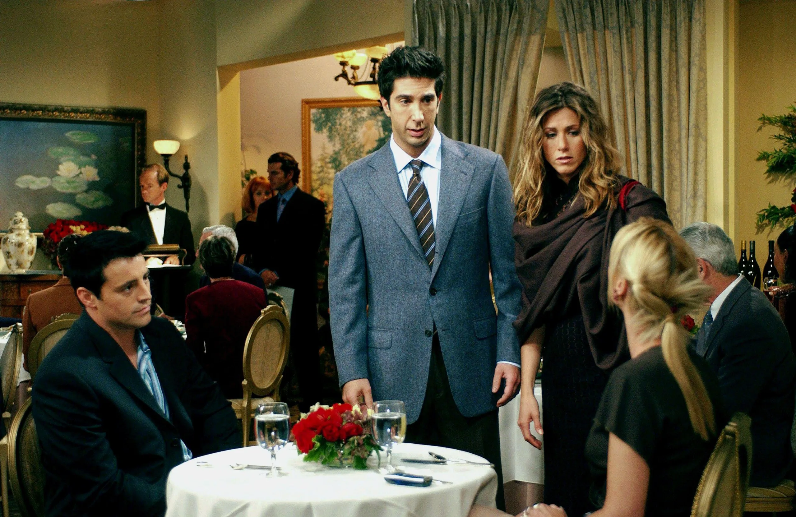 Friends scene with Ross and Rachel in a restaurant talking to Phoebe and Joey who are sat at a table with a yellow wall and curtain background