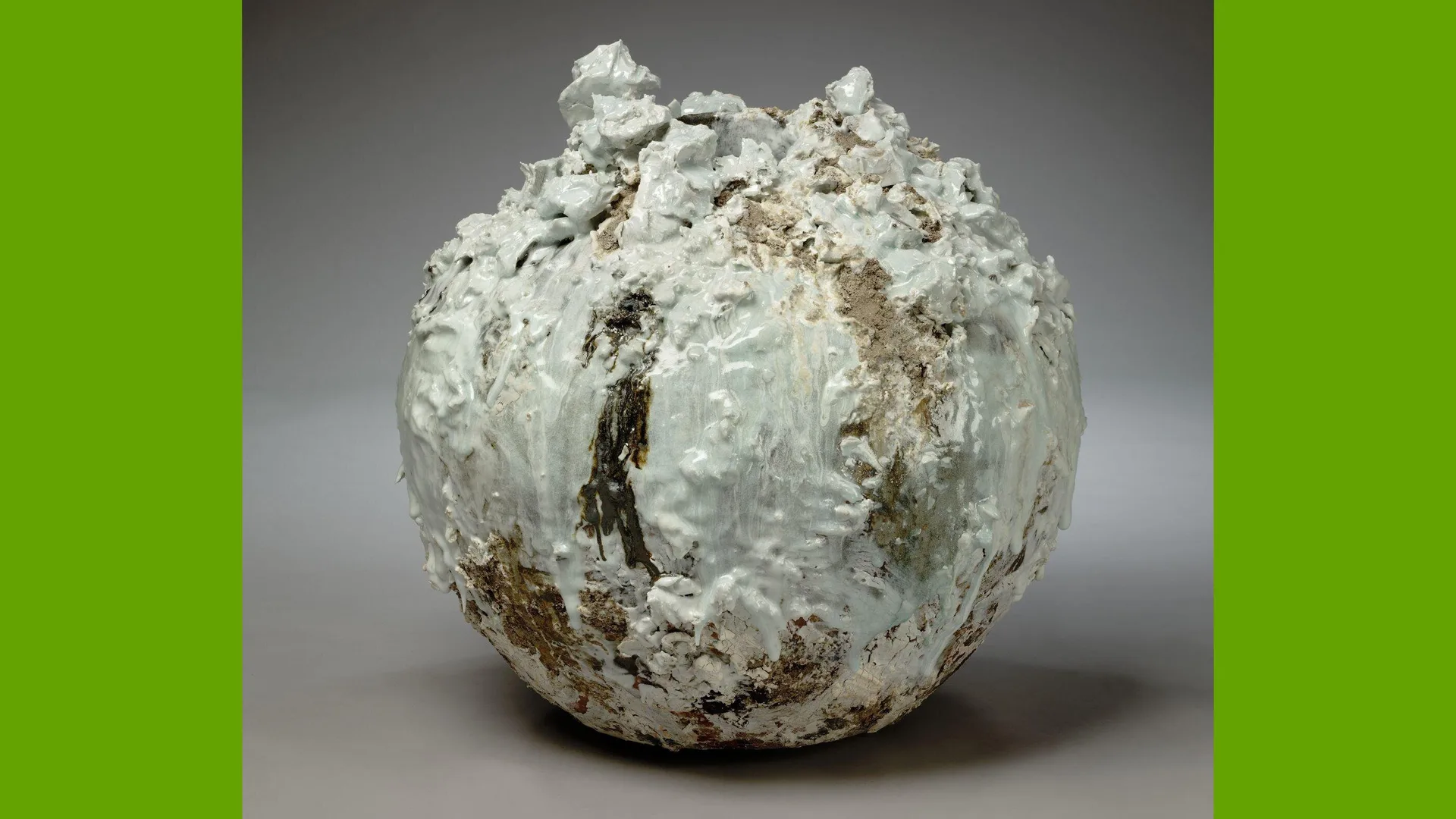 A photo of a V&A object of a white and grey stone sculpture that has a jagged rough surface against a grey background