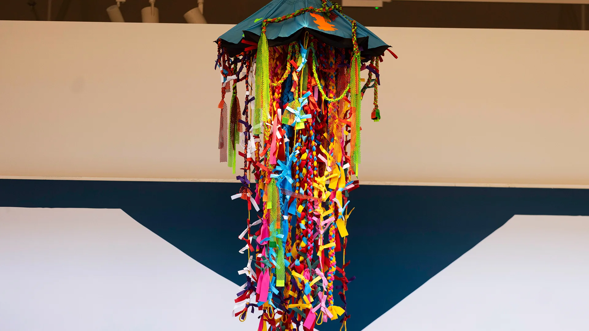 A 3d Yōkai monster is suspended from the ceiling of the Young V&A museum. It looks like a jellyfish with long fabric tentacles and an umbrella for a head.