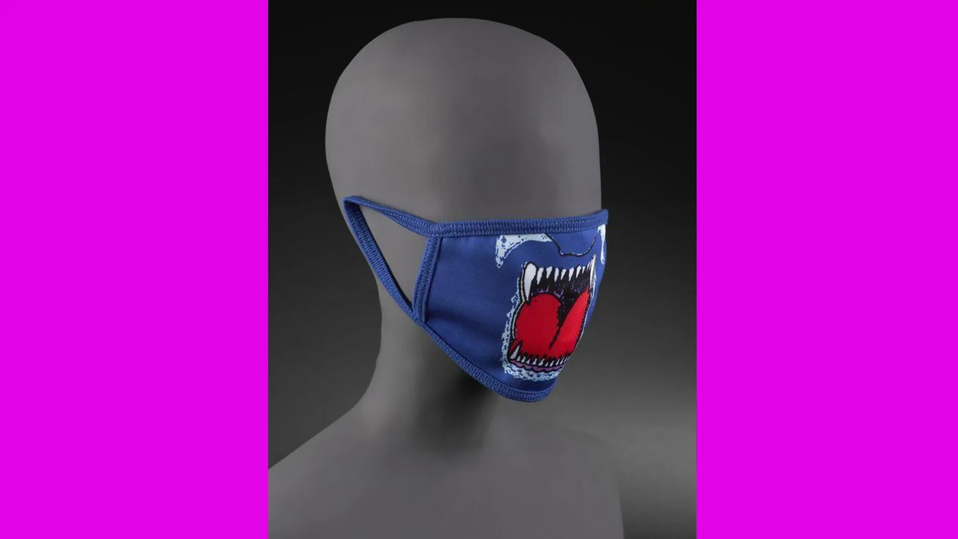 A photo of a navy blue face mask showing an open mouth with red tongue and white fangs on a grey mannequin head