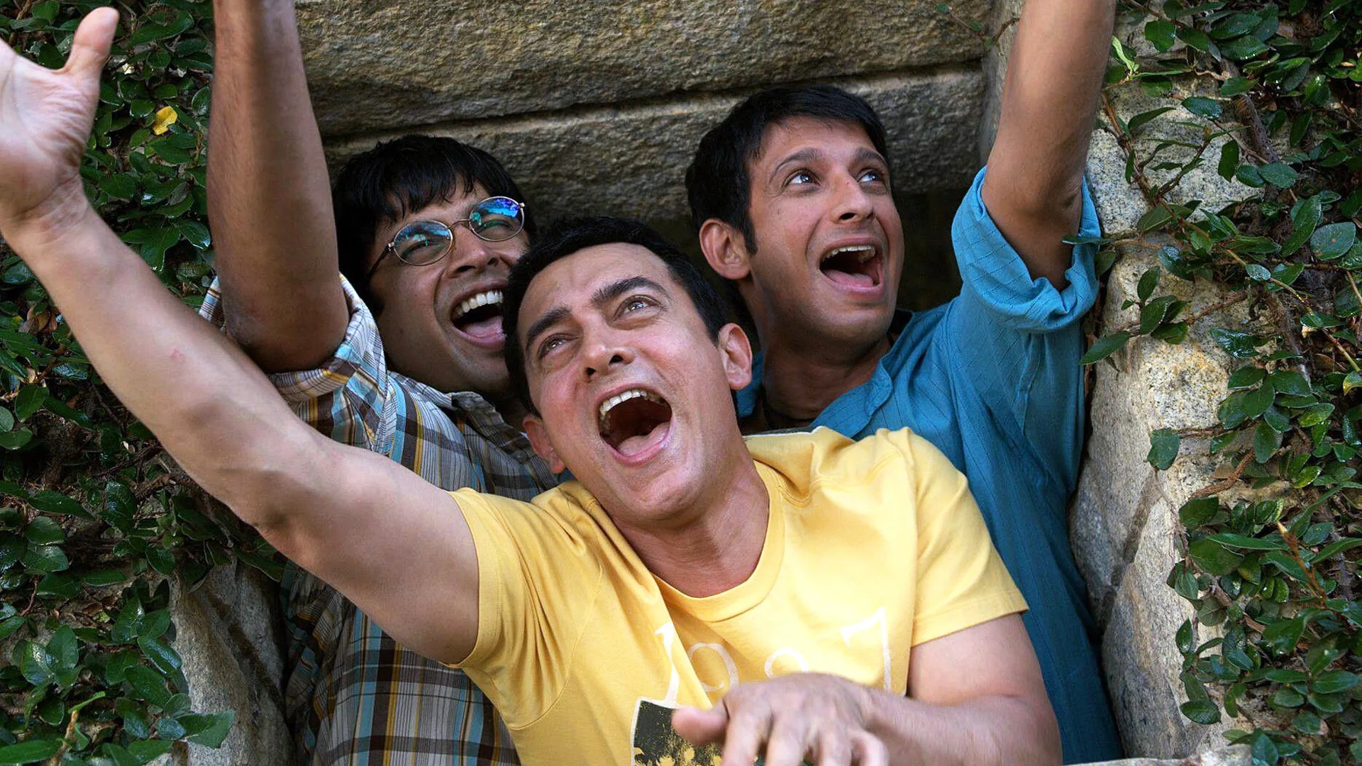 A photo of three men cheering up to something with arms outstretched wearing colourful tshirts