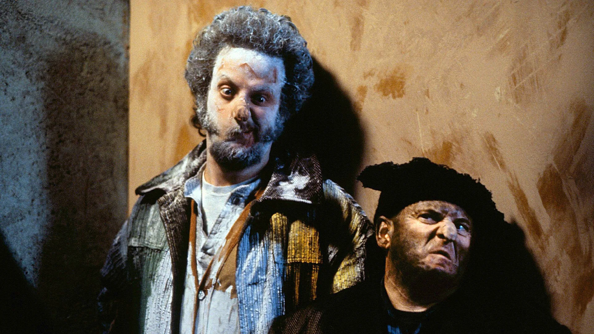 A scene from a Christmas film showing two men with dirty faces and angry, confused expressions against a wooden wall.